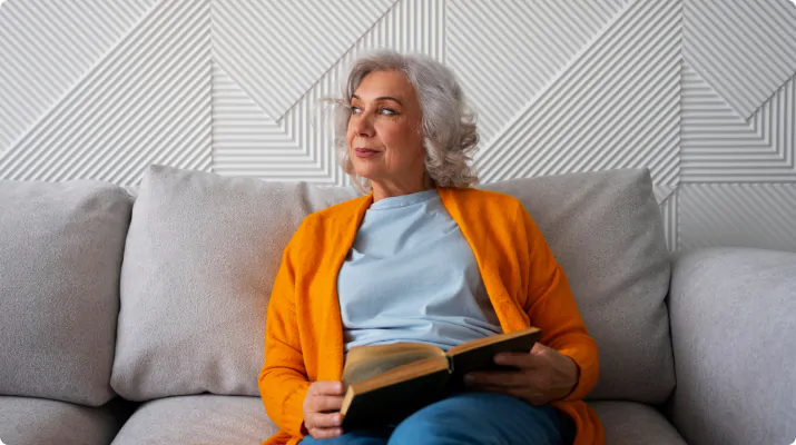 Older woman reading a book on a sofa