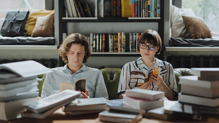 Two people reading books in a cozy room with bookshelves.