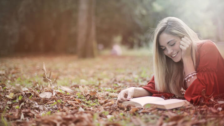 Woman lying on autumn leaves reading a book outdoors.