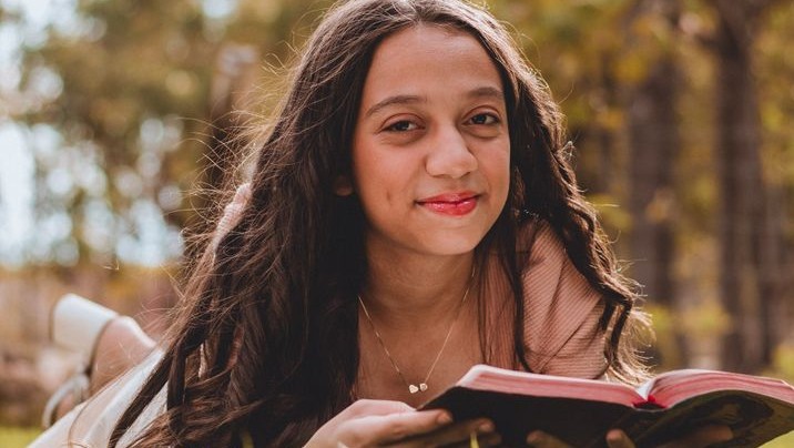 Young woman lying on grass outdoors, reading a book.