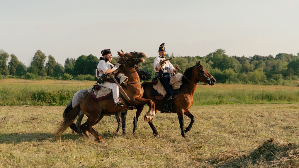 Two horse riders in traditional attire engage in a mock battle.