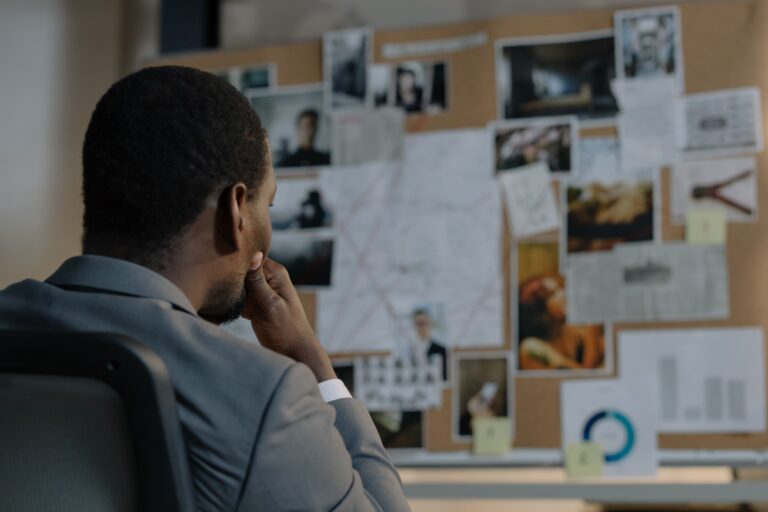 Person analyzing a board with photos and notes connected by lines.
