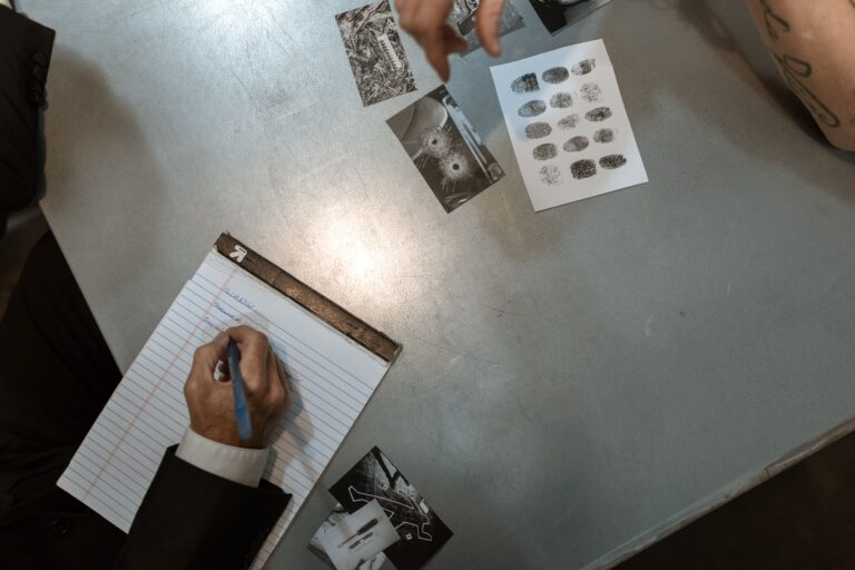 Person writes notes beside crime scene photos and fingerprints