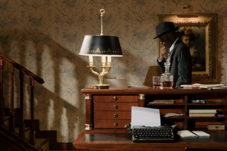 Man in suit and hat stands by a desk with a typewriter
