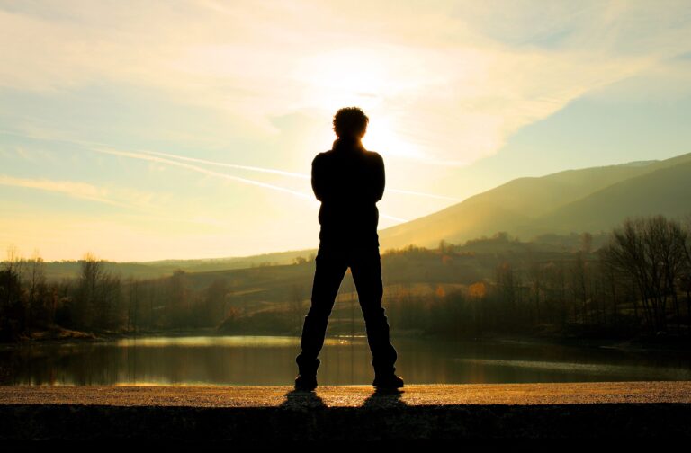 Silhouette of person standing by a lake during sunset