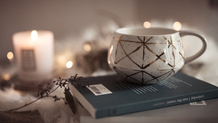 Decorative mug on a book with a lit candle in the background.